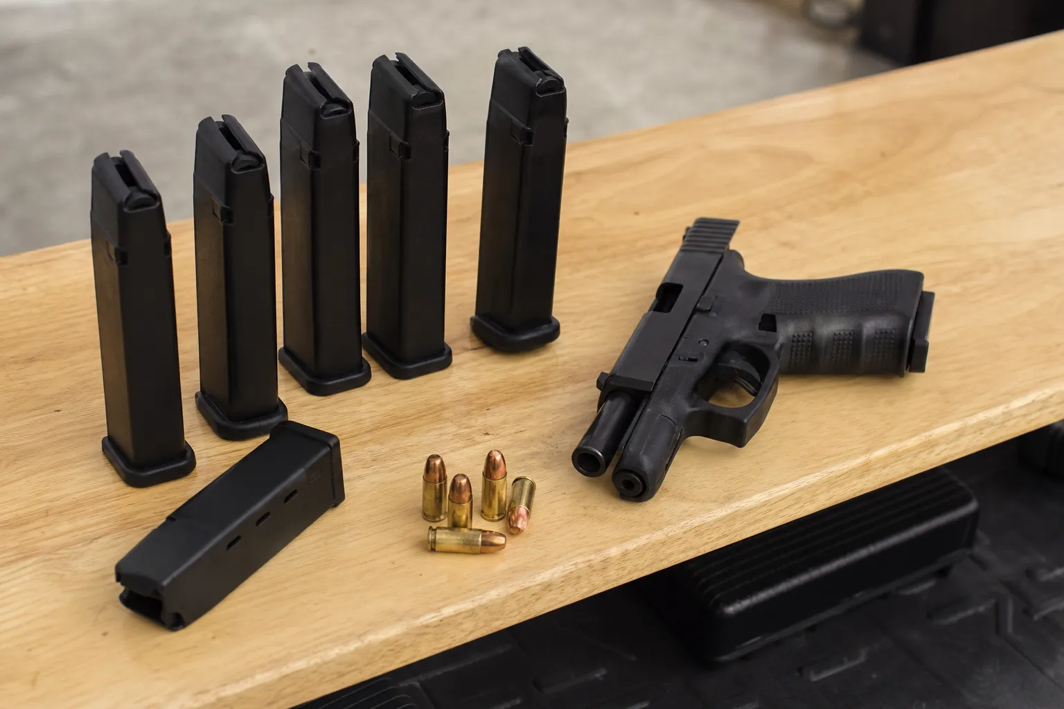 An unloaded handgun lies on a table beside several generic pistol magazines and loose dummy cartridges.