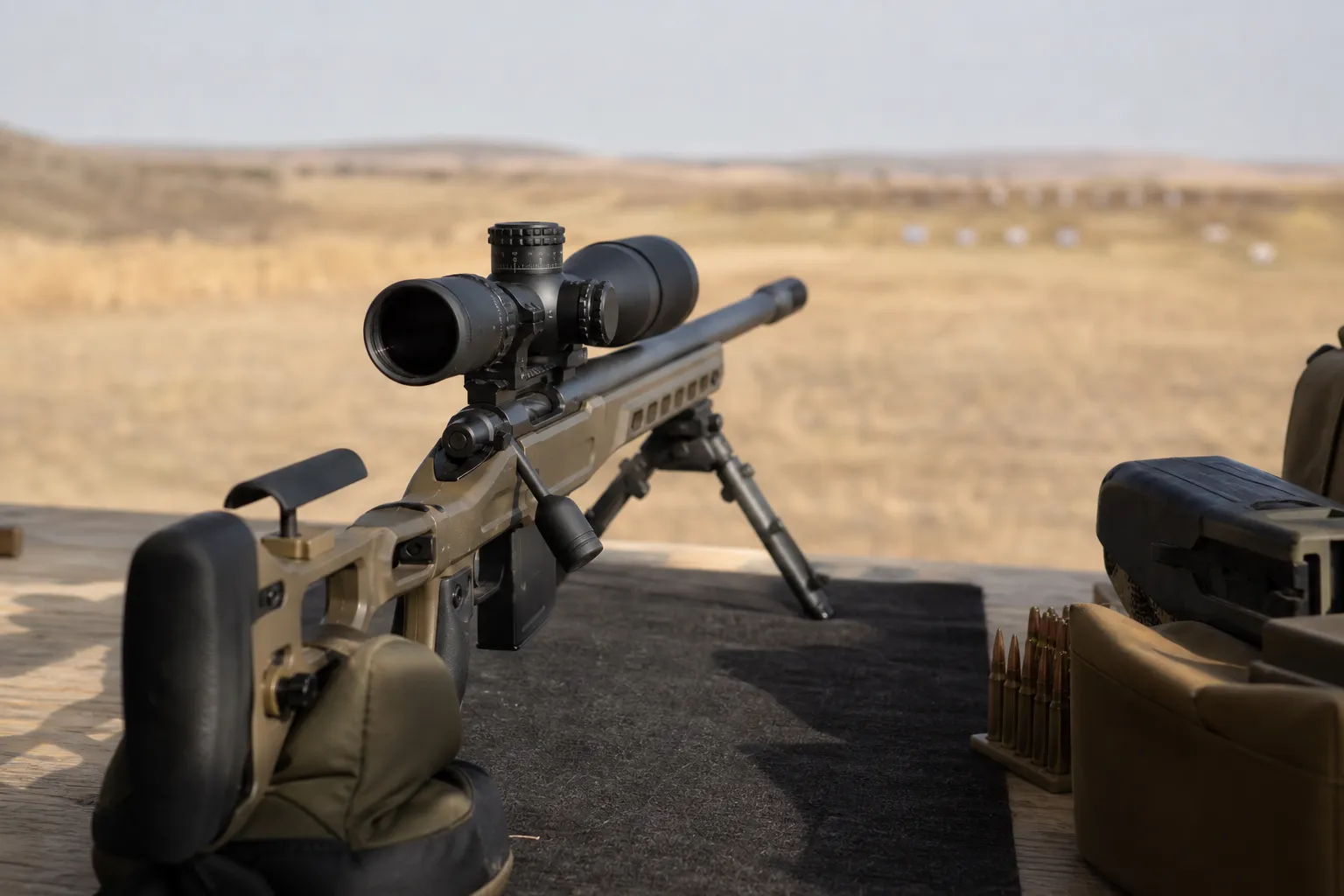 A precision rifle with a scope resting safely on a bench at an outdoor range.
