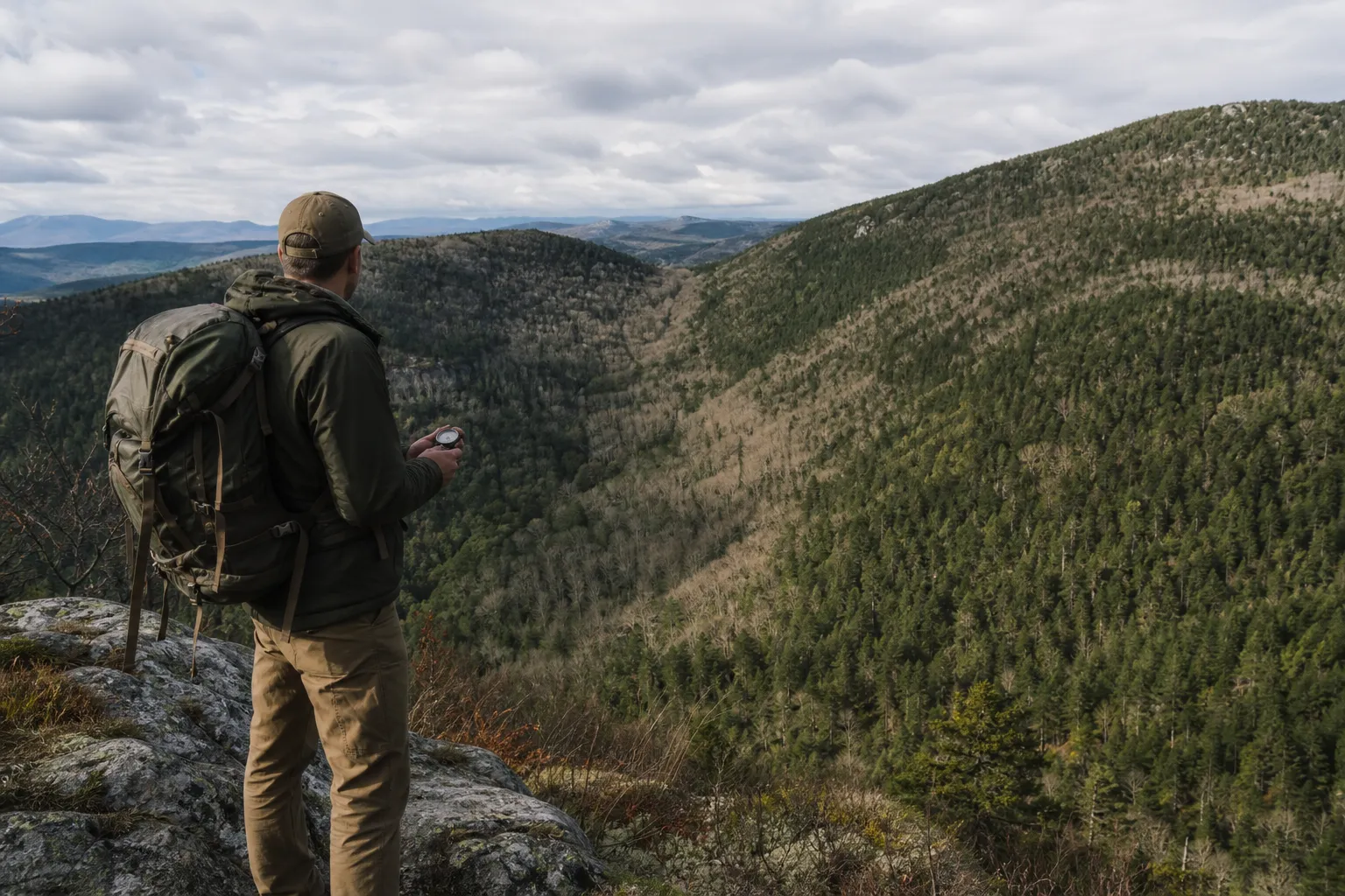 A hiker looks over a landscape with hills, a valley, and a ridgeline.