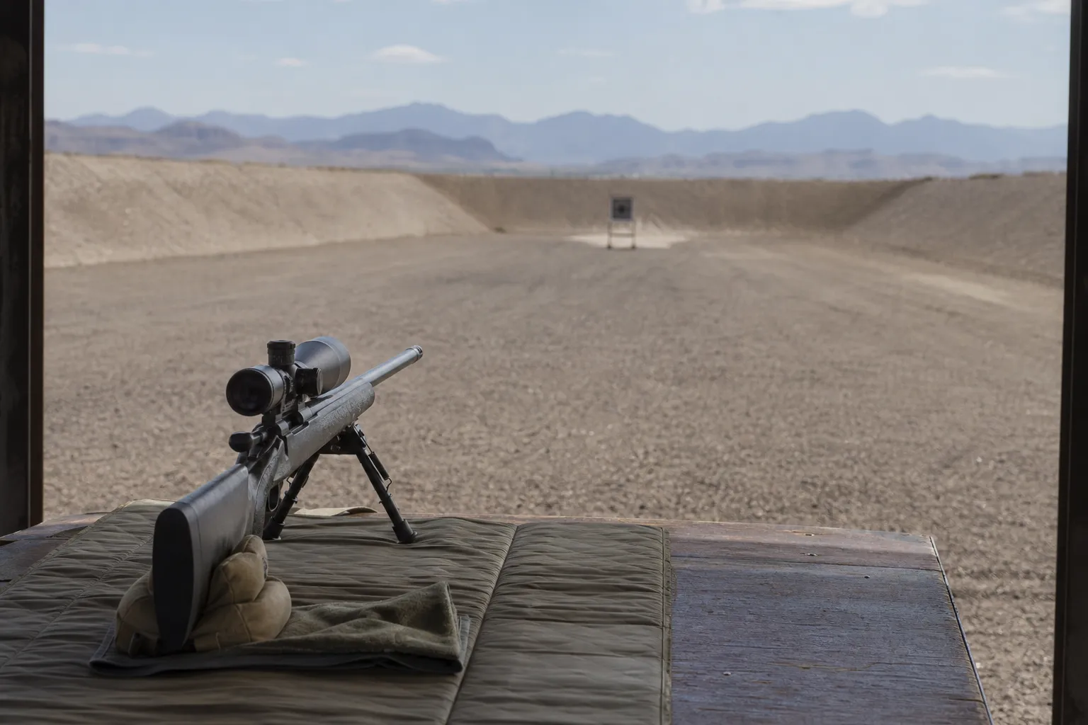 A rifle on a bench points safely downrange toward a distant target, illustrating that velocity changes over distance.