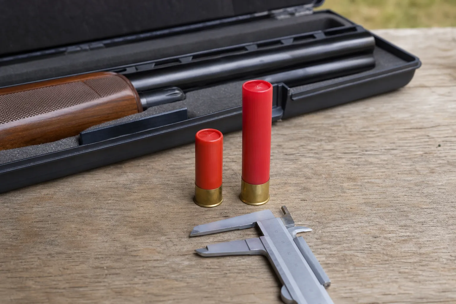 Two different lengths of generic .410 shotgun shells are shown on a table beside a measuring tool for size comparison.