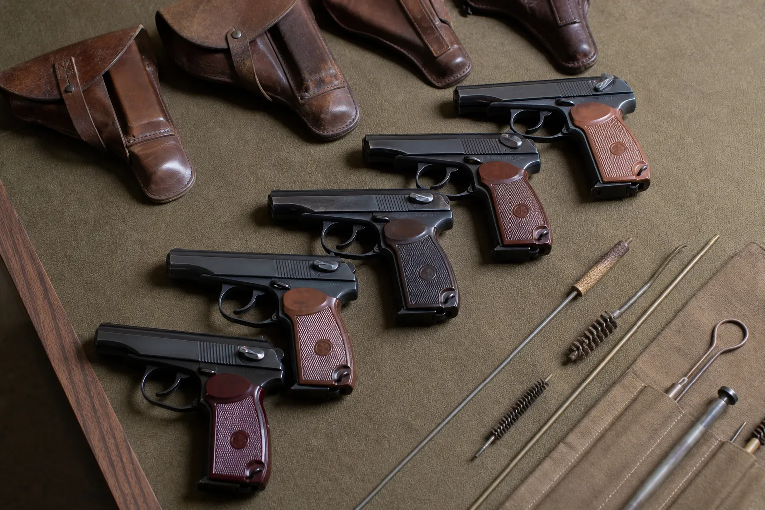 Several similar service pistols and holsters arranged on a table to suggest international production and use.