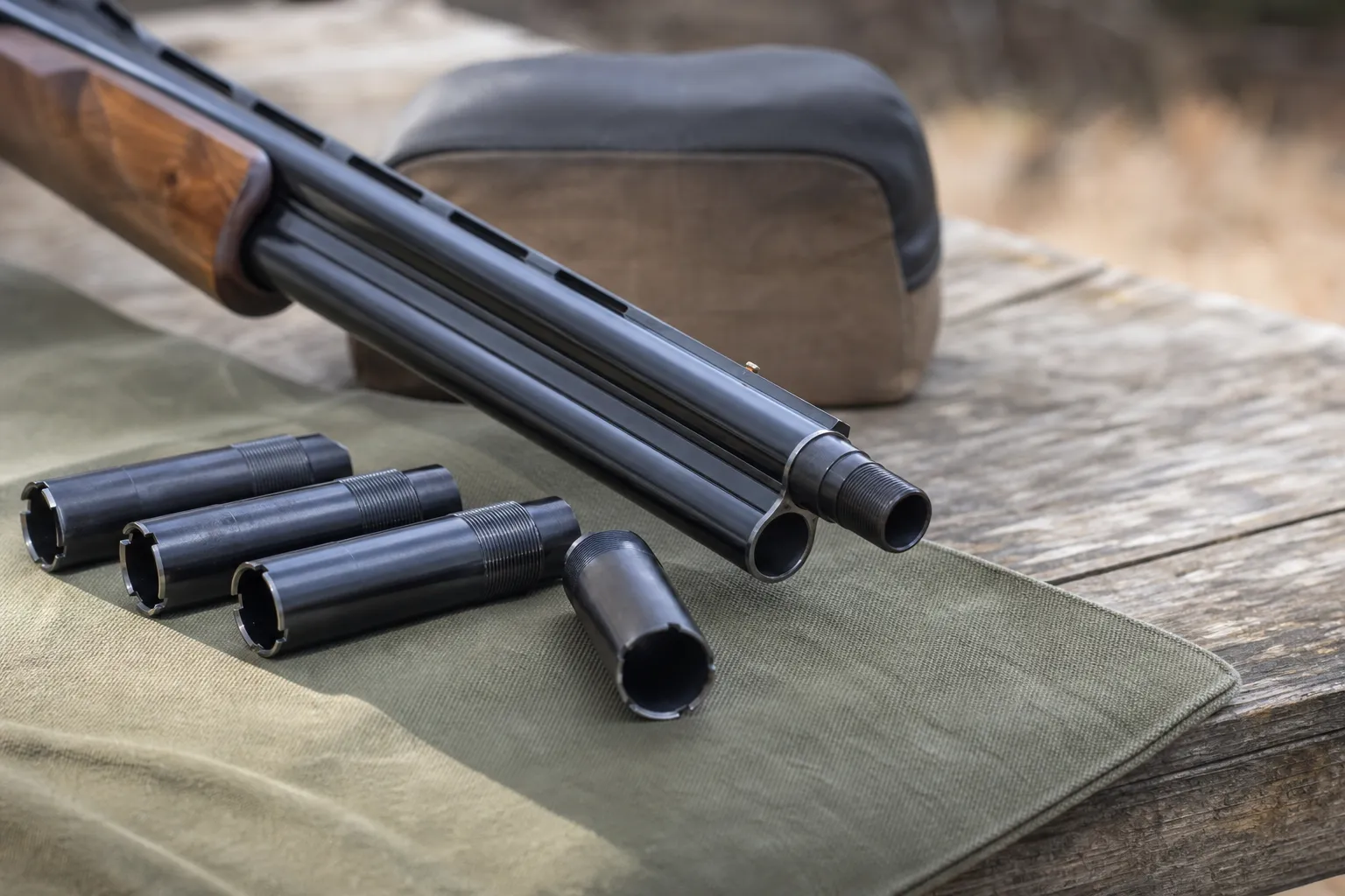 Close view of a shotgun muzzle and removable choke tubes on a bench.