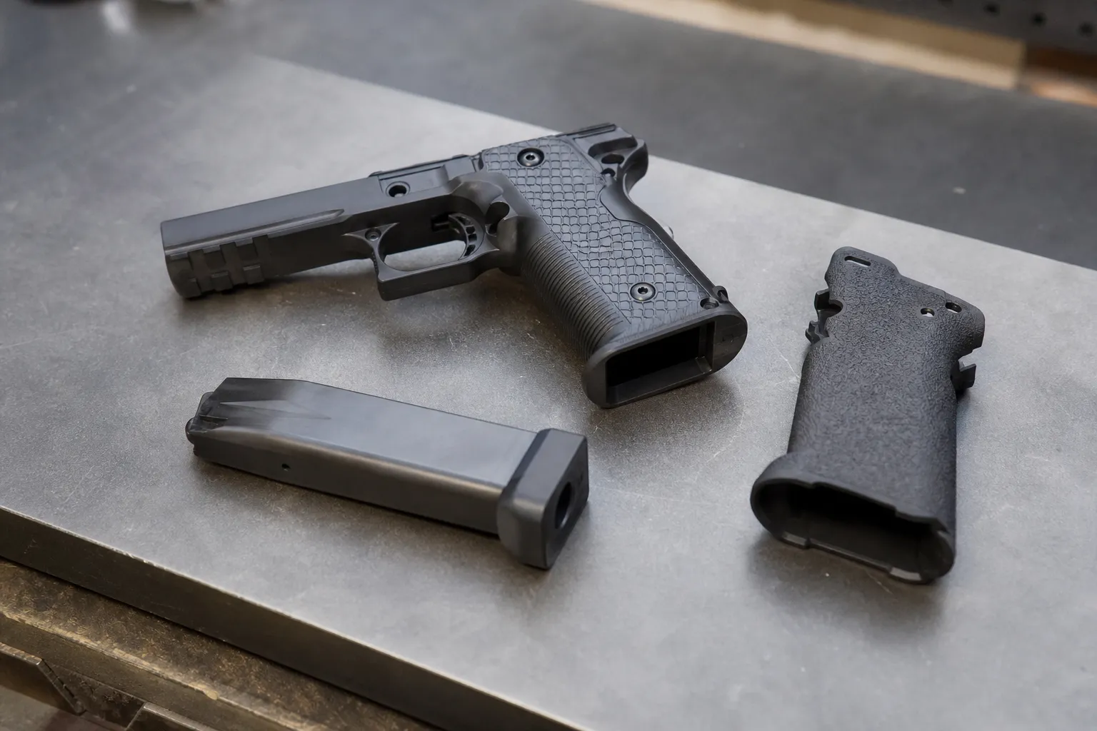 A modular pistol frame, grip module, and magazine arranged on a workbench to show the 2011 concept.